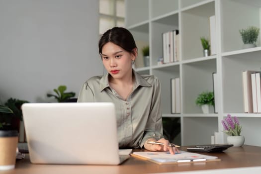 Business woman working in office checking documents. Woman accounting executive using laptop reading paper file financial report, tax invoice.
