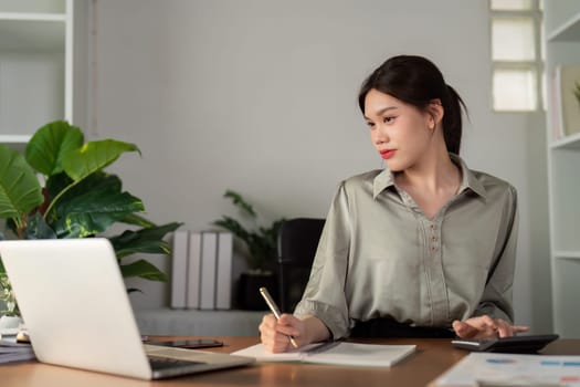 Business woman working in office checking documents. Woman accounting executive using laptop reading paper file financial report, tax invoice.