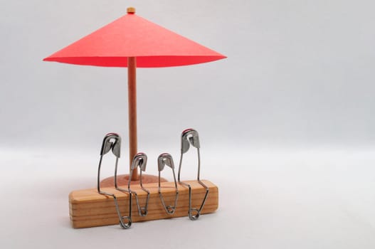 Model safety pin of family sitting on wooden block with red umbrella background. Family insurance concept.