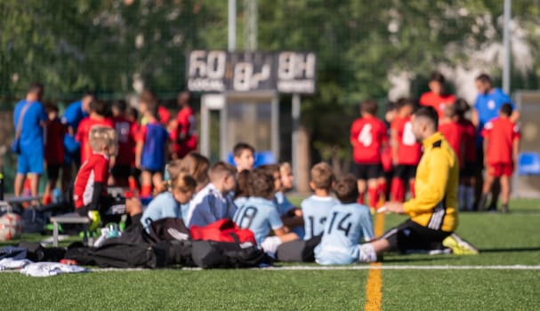 Blurred group of kids soccer players sit on the field listening their coach before the match.