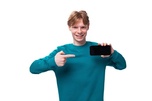 young handsome red-haired man with a blue sweater points a finger at a smartphone.