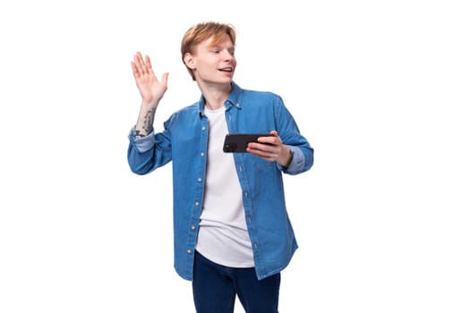 young caucasian man with golden red hair greets with hand holding phone.