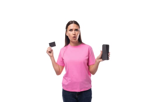 young stylish woman with straight black hair dressed in a pink t-shirt holding a credit card and a smartphone.