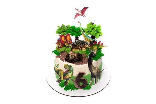 A birthday cake featuring edible dinosaurs and trees as decorations. The cake is brightly colored with various dinosaur species and lush trees, creating a prehistoric scene.