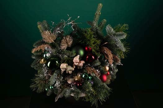 A festive Christmas wreath adorned with colorful ornaments sits on a wooden table. The wreath is crafted with evergreen branches and features shiny baubles, glittering lights, and decorative ribbons.