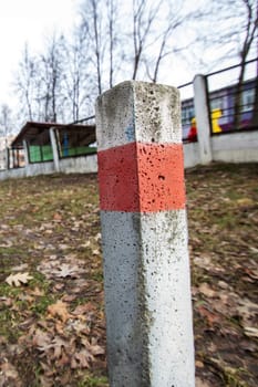 A line of red and white striped concrete poles stand tall against the blue sky, lining the asphalt road surface next to a grassy land lot