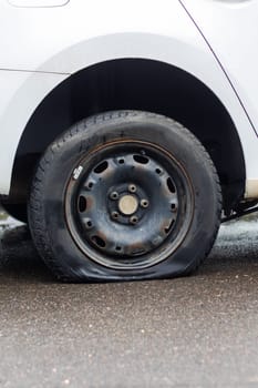 A car with a flat automotive tire on the side of the road, showing its alloy wheel and locking hubs. The tread made of synthetic rubber is visible, with the hubcap missing