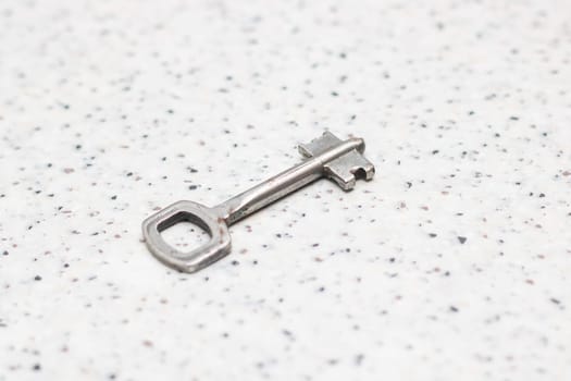 A closeup of a silver key on a white surface, showcasing intricate details and shiny metal. The key can be used as a fashion accessory or as an auto part