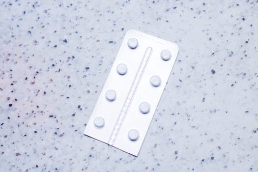 A rectangular blister pack of pills with a circle pattern in electric blue on a plastic sleeve. It sits on a metal counter top, resembling a fashionable accessory