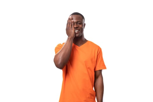 young african man dressed in an orange t-shirt embarrassedly covered his face with his hand.