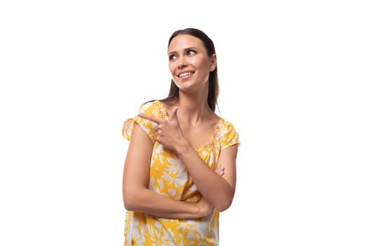 young woman with straight black hair in a yellow sundress with a print pattern smiles on a white background.