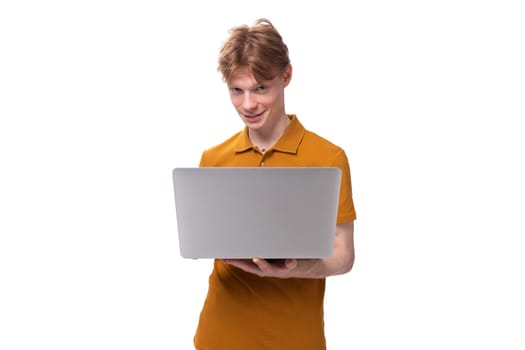 young red-haired guy in an orange t-shirt is studying using a laptop on a white background with copy space.
