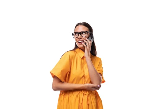 european young brunette lady dressed in an orange summer dress and glasses talking on the phone.