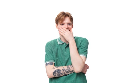 young caucasian man with red hair dressed in a green t-shirt is having doubts and surprise on the background with copy space.