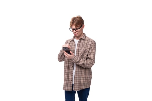young caucasian guy with red hair in glasses and a plaid shirt communicates using a smartphone.