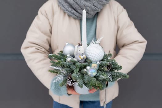A person is holding a festive Christmas arrangement in their hands, showcasing traditional holiday decorations and colors.