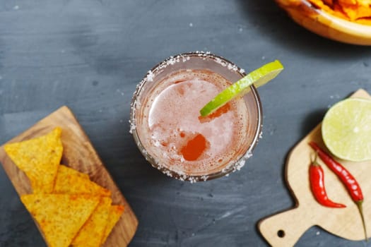 Michelada cocktail with tomato juice, beer and lime in a glass and nachos. Selective focus