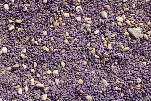 A mixture of purple gravel, rocks, and pebbles is scattered on the ground, blending with the asphalt road surface and soil, creating a unique texture