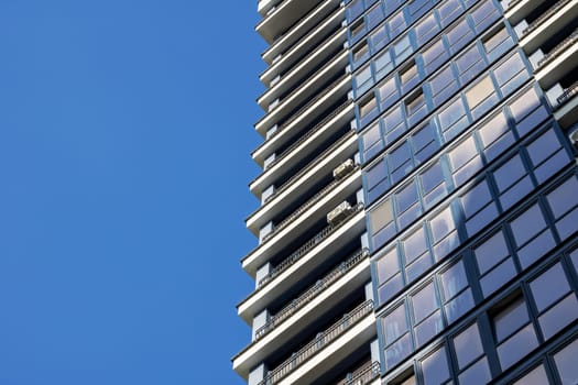 A sleek skyscraper towering against a clear blue sky, surrounded by urban design. The tower block features numerous windows, creating a modern cityscape