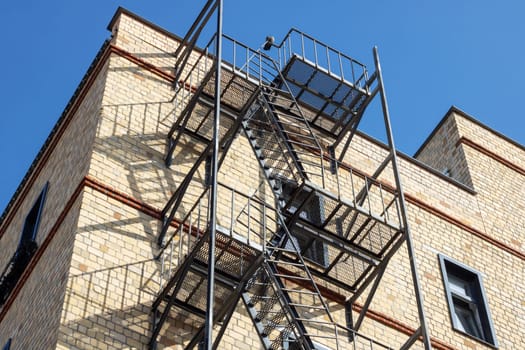 A fire escape made of wood is attached to the buildings facade in the city. It provides an escape route from the condominium through a window to the roof, avoiding overhead power lines