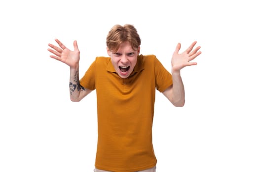 a young frustrated guy with short red hair dressed in a summer orange T-shirt is shouting with his hands up.
