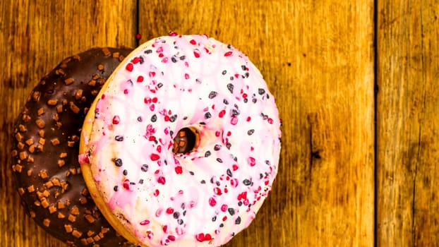 Colorful donuts on wooden table. Sweet icing sugar food with glazed sprinkles, doughnut with chocolate frosting. Top view with copy space