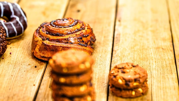 Colorful donuts, puff pastry and biscuits on wooden table. Sweet icing sugar food with glazed sprinkles, doughnut with chocolate frosting. Top view with copy space