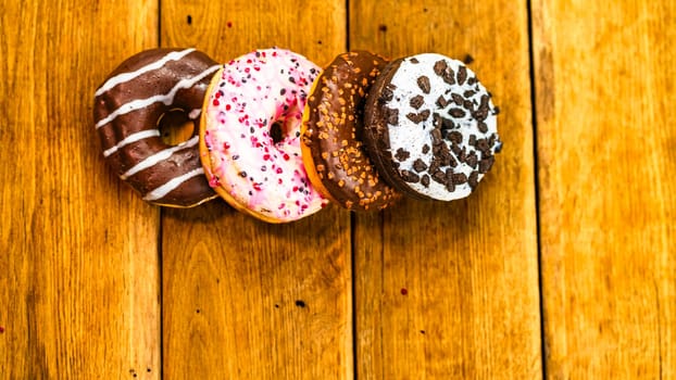 Colorful donuts on wooden table. Sweet icing sugar food with glazed sprinkles, doughnut with chocolate frosting. Top view with copy space