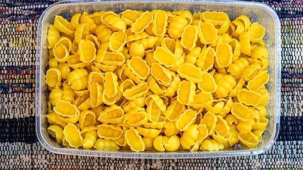 Gnocchi raw Italian pasta in plastic container, close up isolated in rustic composition