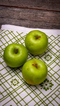 Ripe green apples on a rustic napkin on wooden table.