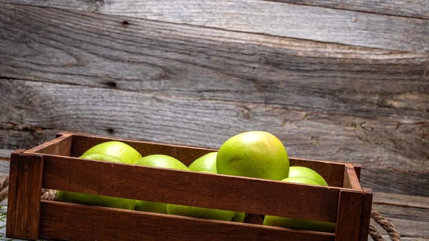 Wooden crate with ripe green apples on wooden table.