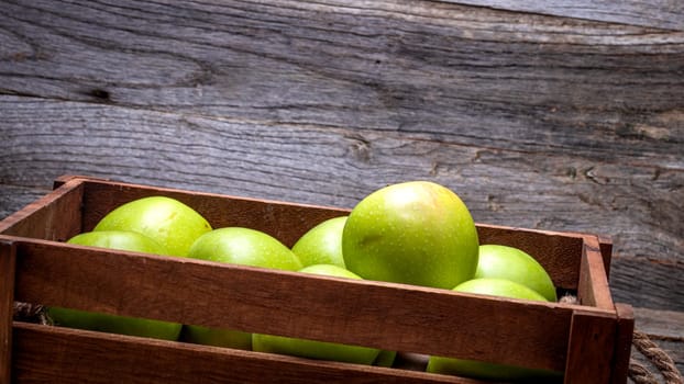 Wooden crate with ripe green apples on wooden table.