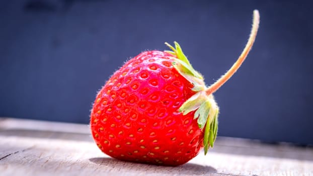 Close up of one strawberry on wooden board isolated on black background