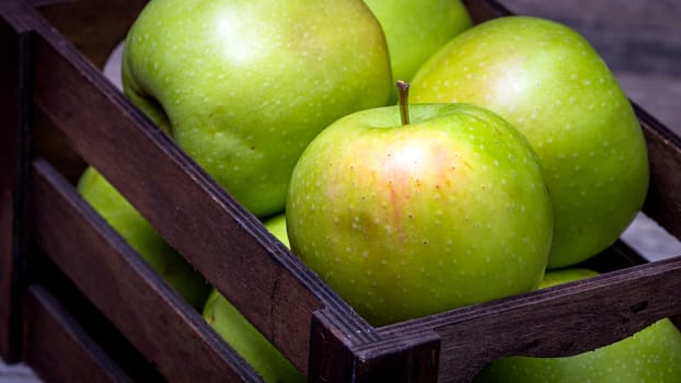 Wooden crate with ripe green apples on wooden table.