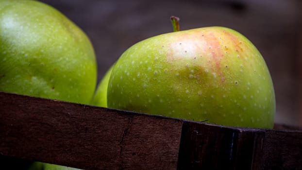 Wooden crate with ripe green apples on wooden table.