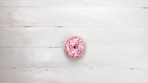 Colorful donuts on white wooden table. Sweet icing sugar food with glazed sprinkles, doughnut with frosting. Top view with copy space