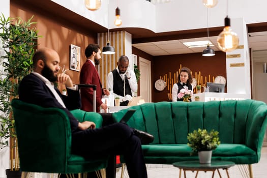 Businessman starting check in formalities, exchanging polite greetings with hotel receptionists at front desk. Company employee eager to see room and prepare for upcoming meetings.