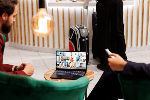 Entrepreneurs use videoconference call in hotel lobby, attending online business meeting before doing check in at reception front desk. Businessmen meet with team on video telework.