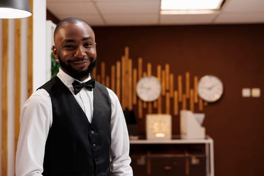Professional hotel worker at front desk, on duty to greet guests and ensure comfortable stay at luxury resort. African american bellhop providing necessary information and services for tourists.