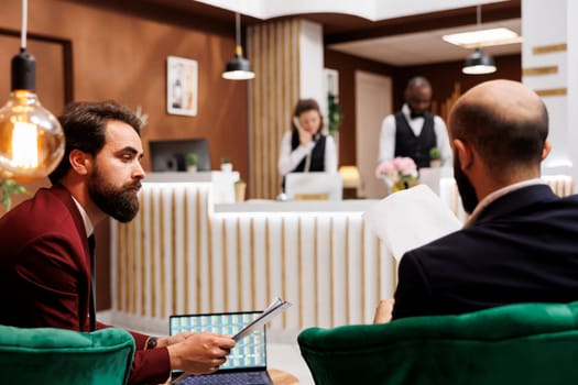 Business travellers conducting global scale project, meeting in hotel lounge area while they travel for work. Entrepreneurs looking to expand horizons, embracing new growth opportunities.