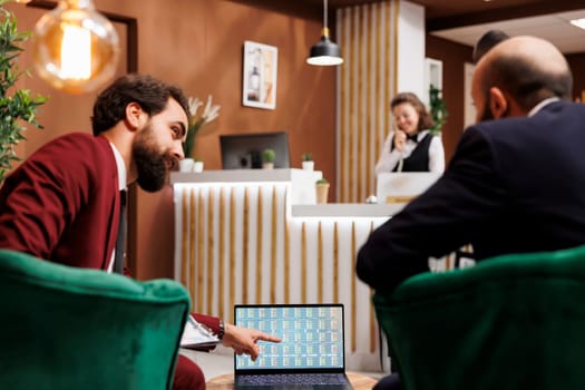 Hotel reception serves as backdrop for business trip, representing exchange of ideas and common goals to forge connections. Businessmen negociating terms of a partnership, laptop notes.