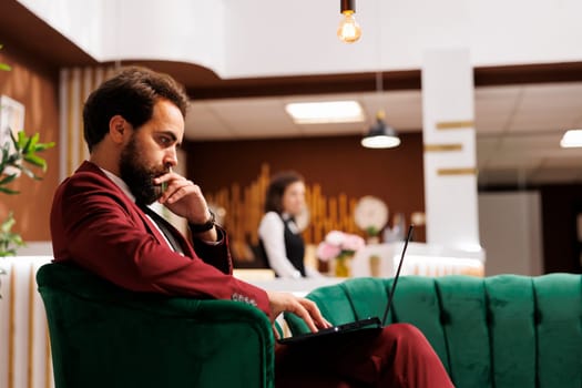 Company manager on business trip preparing to attend meeting in lounge area at hotel. Businessman waiting in reception lobby, checking presentation on laptop before starting conference.