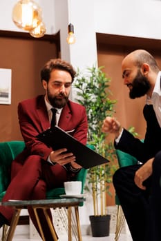 Management team review notes in lobby, preparing for upcoming international business meeting at luxury hotel. Two colleagues travelling for work trip, check conference speech on papers.