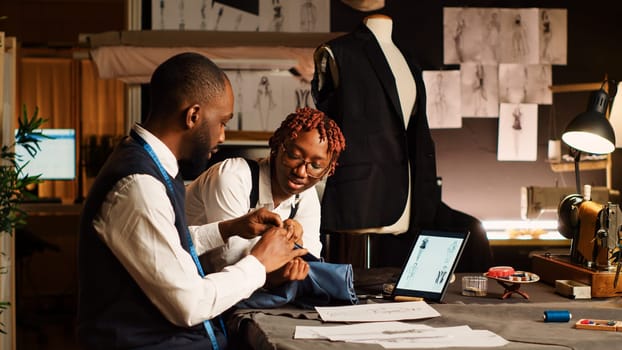 Two tailors choosing fabric for clothes in workshop, looking at materials on workstation before creating fashion collection. Team of couturiers crafting items with needlework.