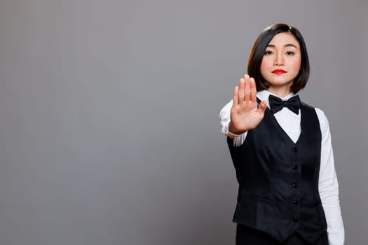 Serious asian waitress showing stop symbol with hand and looking at camera with confident face expression. Catering service woman employee making rejection sign with arm portrait