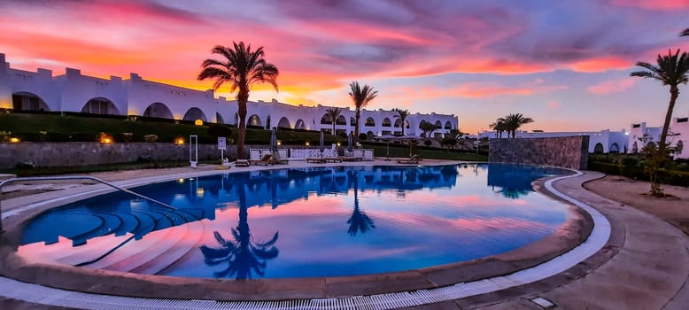 Beautiful sunset at Marsa Alam, Egypt - April, 2024: Pool area of the Hotel Hilton by the Red Sea. Many palm trees are reflected in the calm water of an empty swimming pool. High quality photo