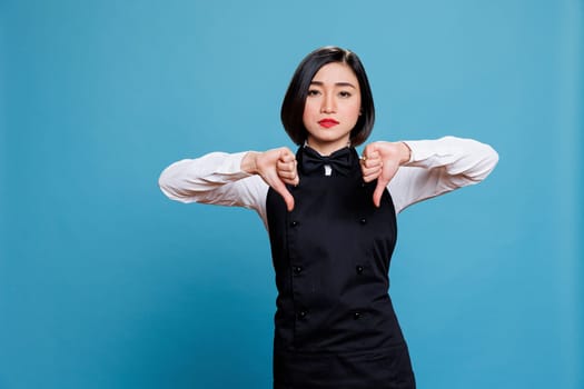 Waitress showing negative feedback and dissatisfaction with thumbs down gesture and looking at camera. Restaurant worker showcasing bad customer experience symbol and looking at camera