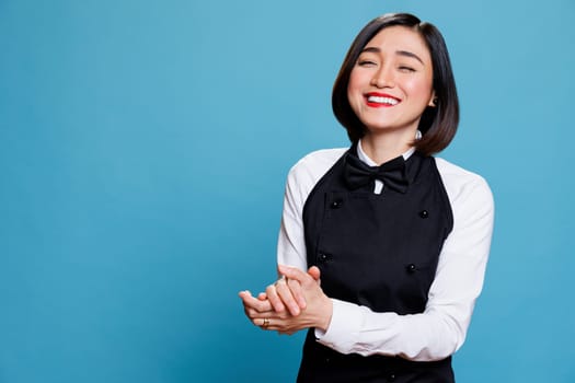 Smiling cafe waitress applauding with joy and encouragement, showcasing appreciation portrait. Attractive woman receptionist clapping hands and laughing while posing in studio