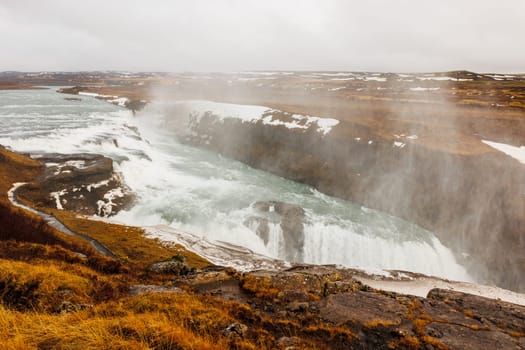 Gullfoss cascade in icelandic scenery, beautiful nordic landscape with snow and freezing cold water falling off cliff. River stream on top of frosty hill, scandinavian waterfall.