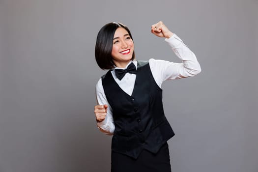 Cheerful asian waitress dressed in restaurant uniform dancing with joyful facial expression. Cafe smiling woman employee making moves with hands and body, spreading happiness